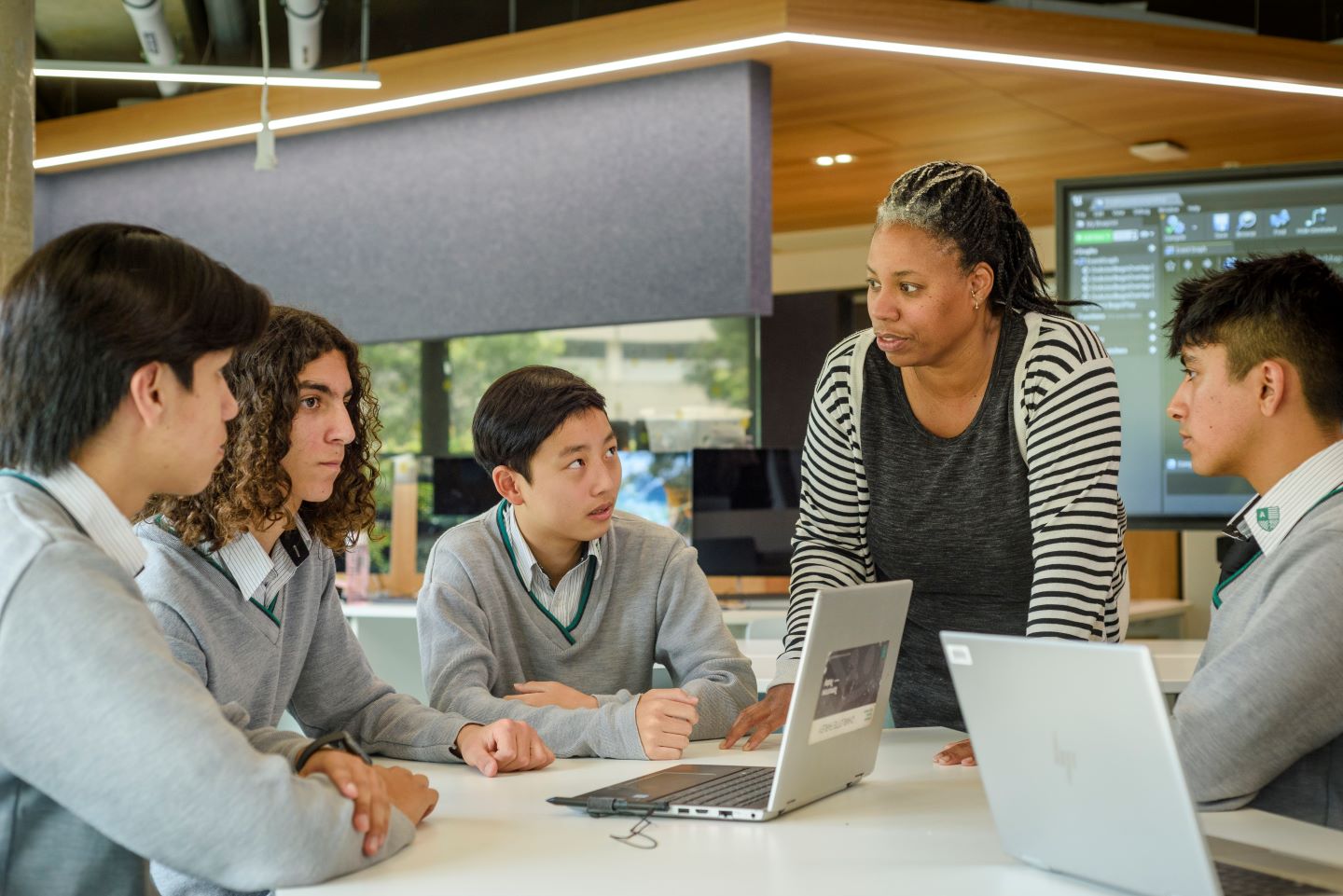 High school students with their laptops being guided by a teacher.