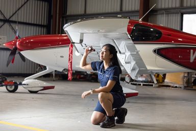 A female student kneeling in front of a small aeroplane