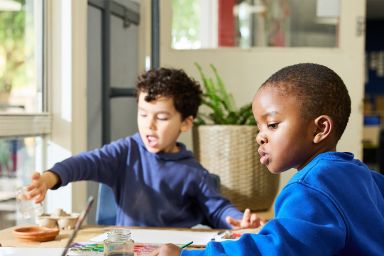 Two students painting paper while seated at a table