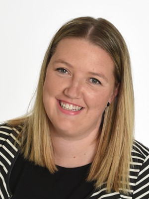 Lauren Jew, 2017 Community Engagement Award. Lauren is smiling, and is wearing a striking black-and-white striped jacket over a black top.